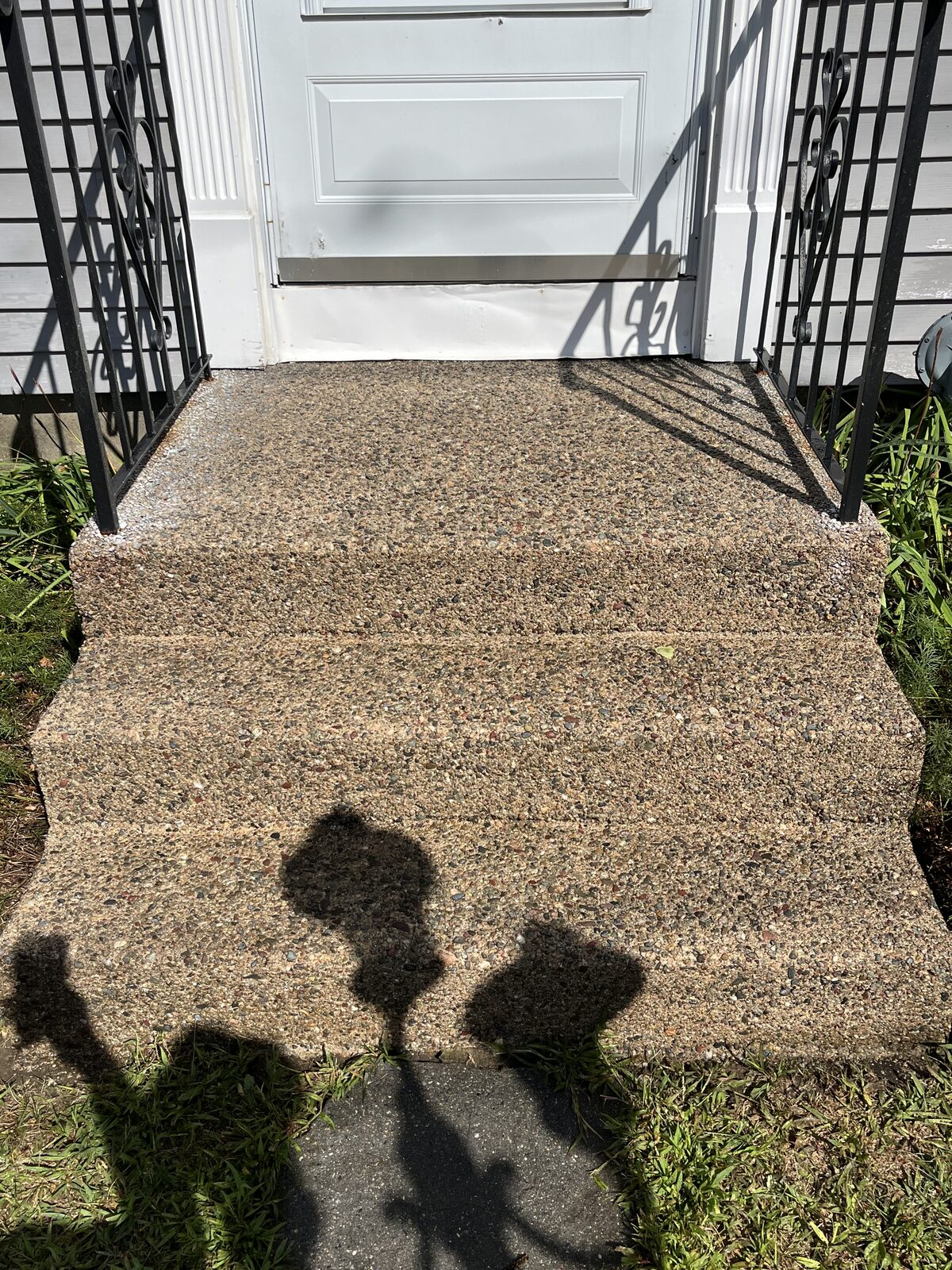 After pressure washing concrete front steps in Attleboro MA showing clean, warm exposed-aggregate steps with the staining and grime washed away between black iron railings
