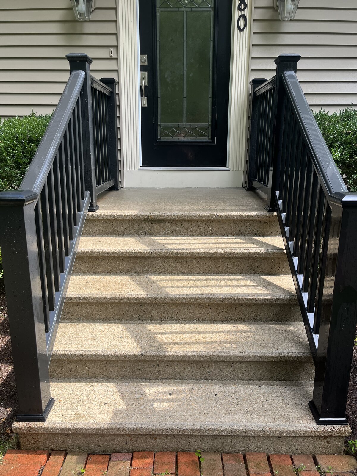 After pressure washing concrete front stairs in Marshfield MA showing clean, bright exposed aggregate steps with the natural glow restored between black railings