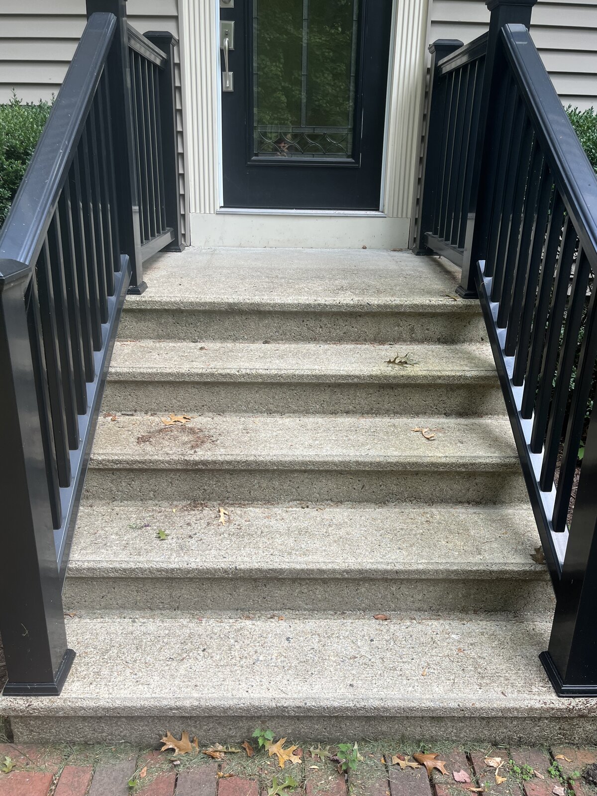 Before pressure washing concrete front stairs in Marshfield MA showing years of dark staining, organic growth, and grime on the exposed aggregate steps between black railings