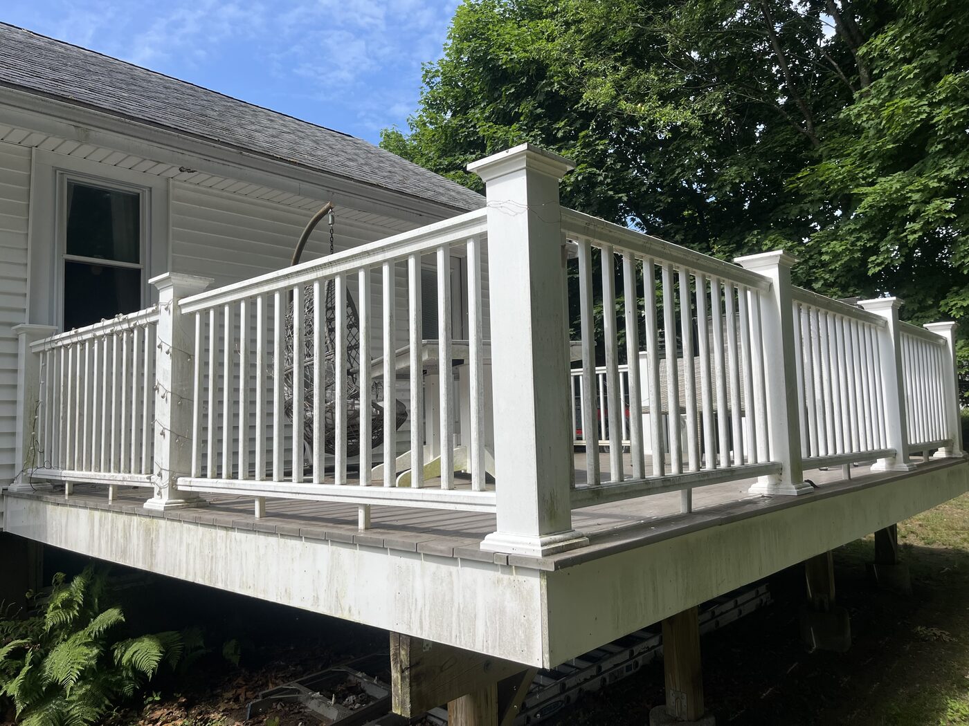 Before cleaning a raised composite deck in Weymouth MA showing gray and green staining on the white railing, posts, and skirt board beside the home