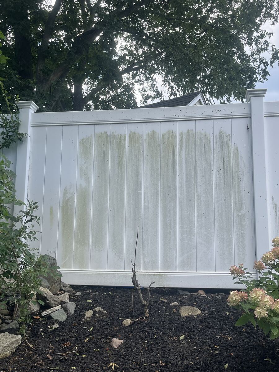 Before fence cleaning in Hingham MA showing green algae streaks on white vinyl privacy fence