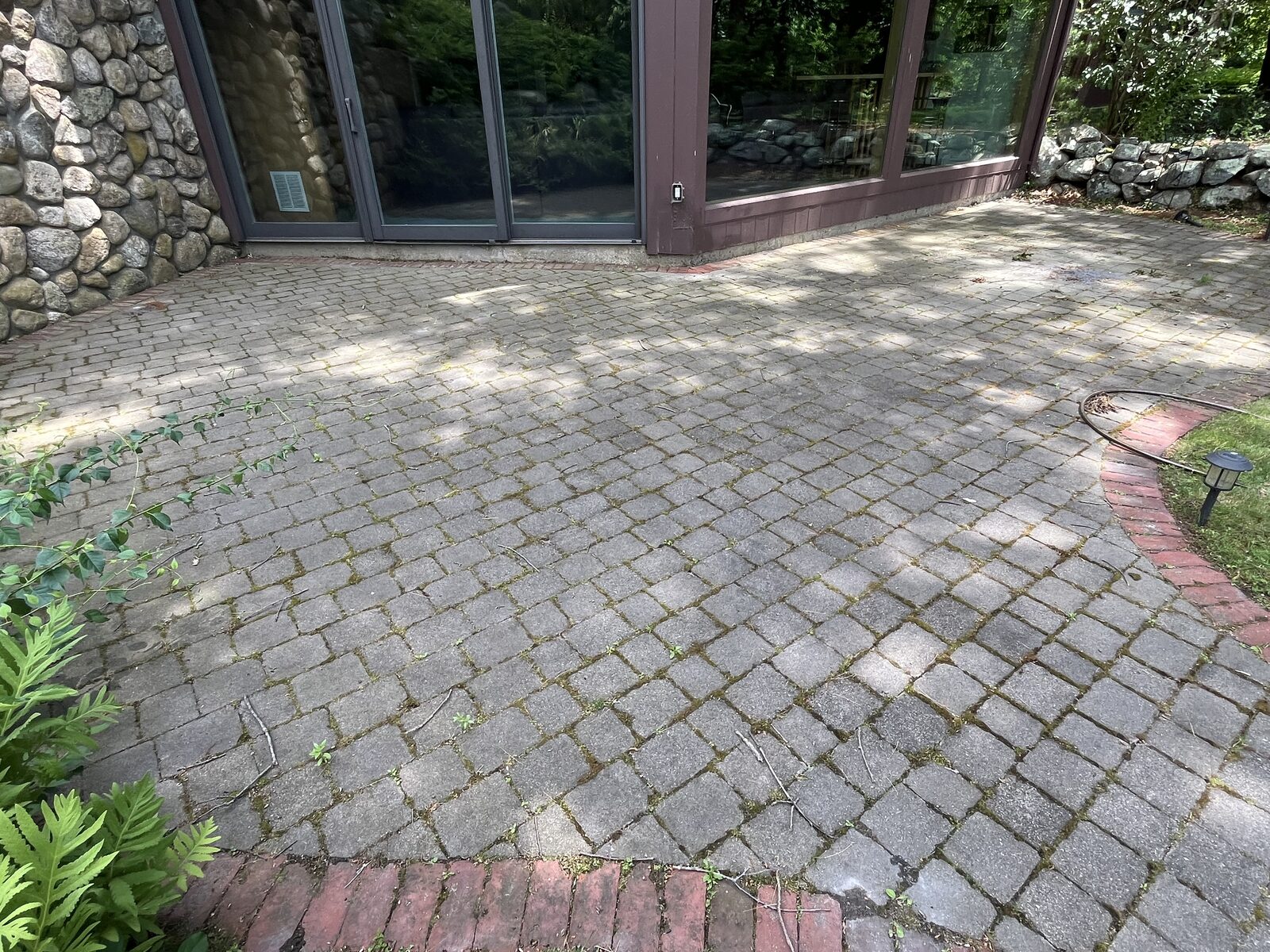 Before cobblestone paver patio cleaning in Marshfield MA showing moss, weeds, and dirt built up in the paver joints by the house