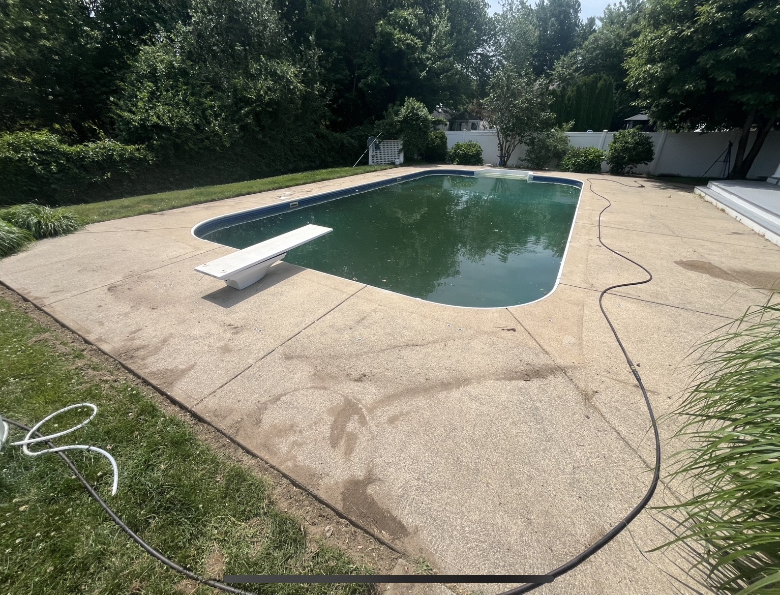 Before pool deck cleaning in Marshfield MA showing dirt streaks and grime on the exposed-aggregate concrete around the pool