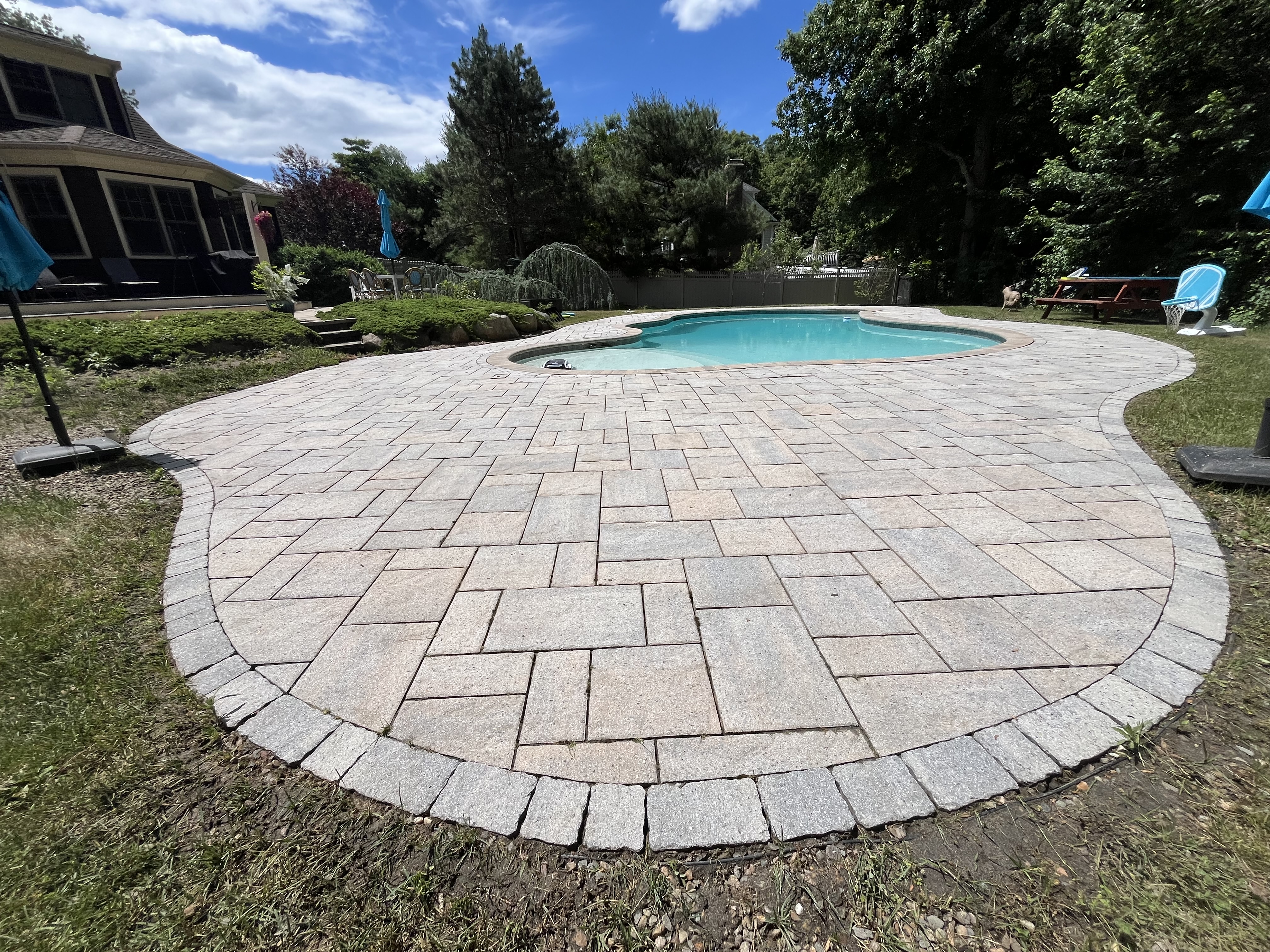 After paver pool deck cleaning in Scituate MA by H2WOAH Exterior Cleaning showing clean restored stone pavers around a kidney-shaped pool