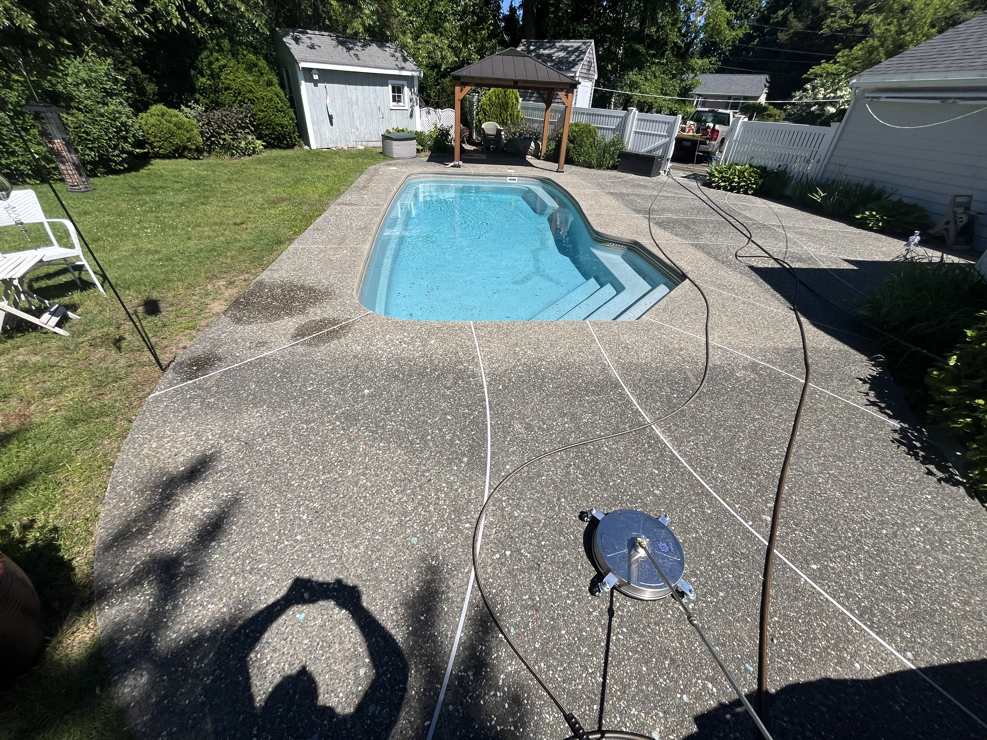 Before pool deck cleaning in Marshfield MA showing dull, dirty exposed-aggregate concrete with algae and grime around the pool
